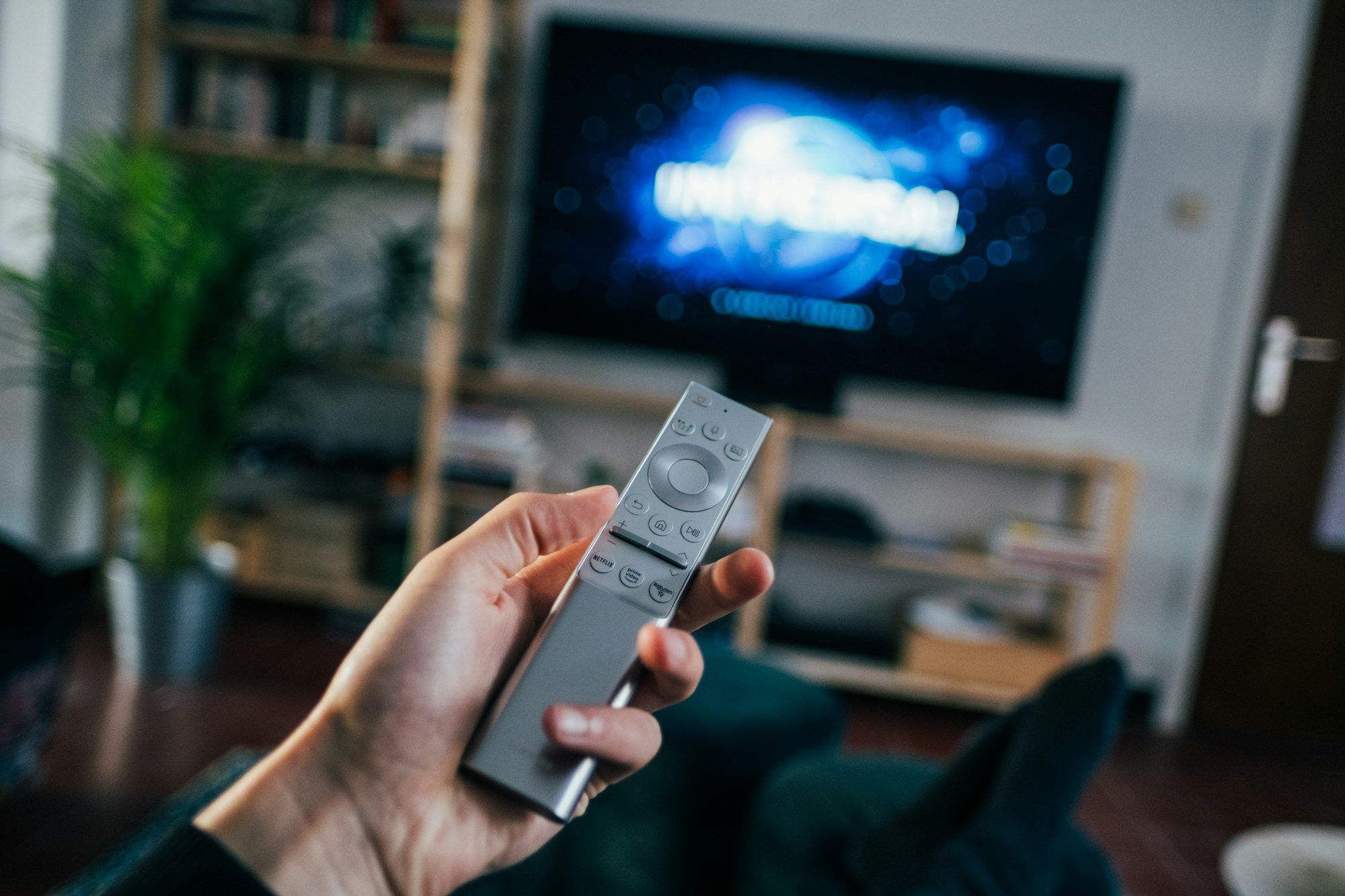 Hand met een afstandsbediening, op de achtergrond een tv