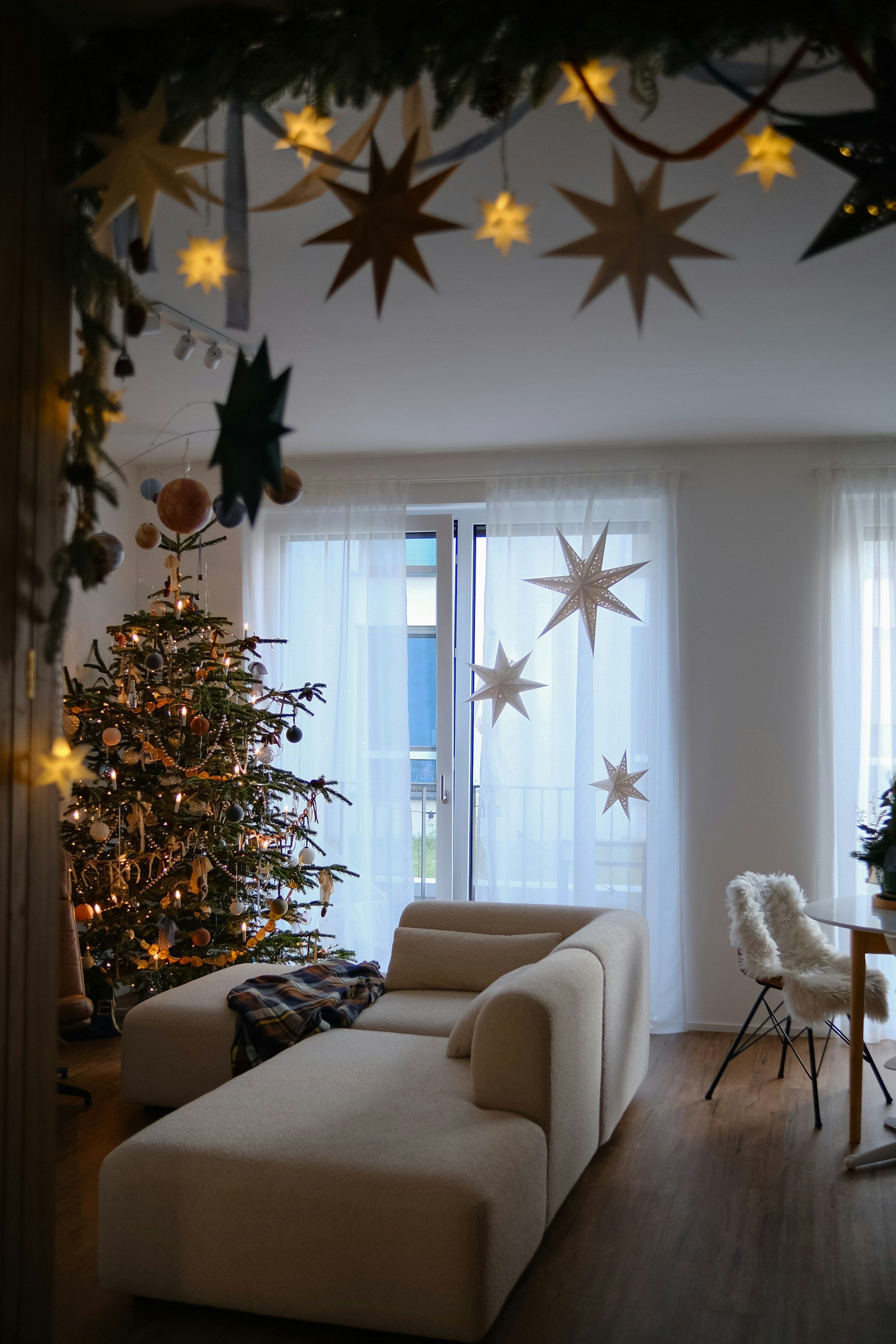 Woonkamer met een verlichte kerstboom en papieren sterren voor het raam