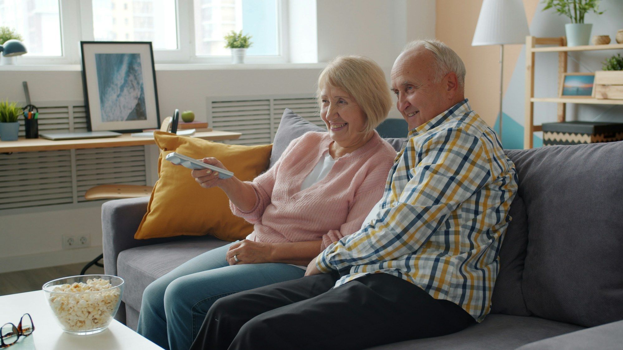 Ouder stel kijkt samen tv met een bak popcorn op tafel